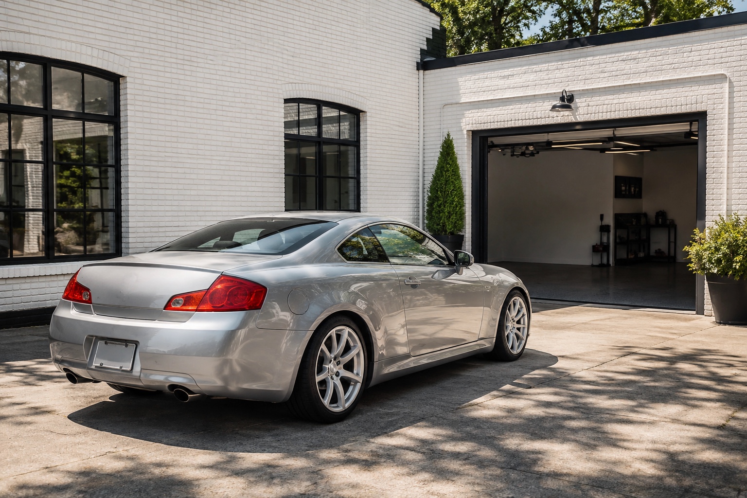 A polished silver coupe in daylight outside a white-brick detailing workshop